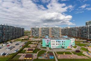 Modern residential complex with multi-story buildings, parking, and a bright kindergarten building with playgrounds. photo
