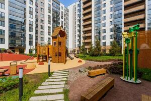 Landscaped courtyard of a residential complex with a wooden playground, benches, and green spaces. photo