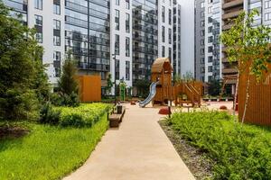 Landscaped courtyard with a wooden play complex, a path, and bushes against the background of multi-story buildings. photo