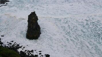 A lone person standing on top of a rock in the ocean photo