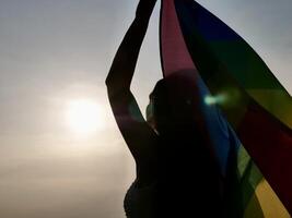 A woman holding a rainbow flag in the sun photo