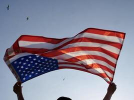 A man holds an american flag in front of a plane flying over the us flag photo
