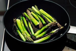 Fresh asparagus cooking in a skillet on a stovetop in a modern kitchen photo