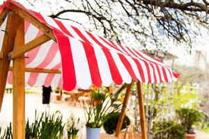 Colorful striped awning at an outdoor garden setting with dining tables and greenery photo