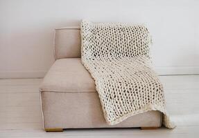 Cozy modern sofa with knitted blanket draped over it in a minimalistic interior setting photo
