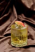 Alcoholic cocktail with ice and apple on brown satin background photo