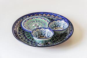 Ceramic dishes featuring intricate oriental patterns, characterized by vibrant blues, greens, and whites. A large circular plate serves as the base with three smaller bowls on top. photo