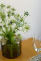 a bouquet of daisies in a glass vase stands on a table on a white background, a wine glass on the table, depth of field, side effect, defocus, macrophotography, bokeh photo