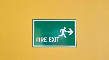 Green fire exit sign or board on yellow wall background for giving direction to exit when have fire in building or place. photo