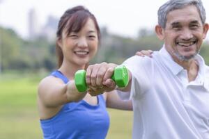 senior man doing exercise with dumbbell with trainer elderly having physical activity in the park photo