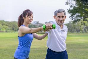 senior man doing exercise with dumbbell with trainer or physiotherapist,elderly having physical activity in the park photo