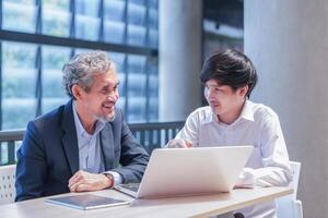 senior professor sitting and giving advice student with laptop computer in university,young asian man conversation with advisor teacher photo