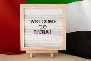 Message text WELCOME TO DUBAI on background of waving UAE flag made from silk. United Arab Emirates flag with concept of tourism and traveling. Inviting greeting card, advertisement. Dubai welcoming card photo