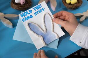 Person holding handmade greeting card with message HOLD THE EARS STIFF written in beautiful handwriting. Gesture shows excitement and joy for the upcoming event. Springtime holiday gift present zero cost ideas. Creative art preparation photo
