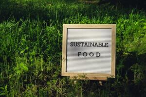 Letter board with text SUSTAINABLE FOOD on background of garden bed with green herb dill. Organic farming, produce local vegetables concept. Supporting local farmers. Seasonal market photo