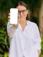 Smiling woman showing smartphone with blank screen outdoor. Mockup for app, website, or social media design. photo