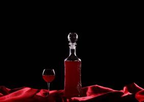 A bottle of red wine and a glass on a table photo