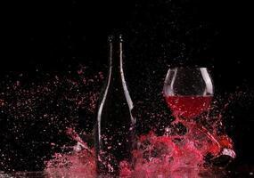 A bottle of red wine and a glass of red wine splash on a black background photo
