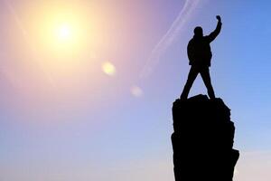 Silhouette of a man standing on top of a mountain with his arms raised photo