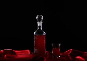 A bottle of red wine and a glass on a red cloth photo