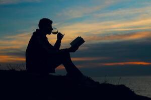 A man sitting on a hill with a book and a glass of wine photo