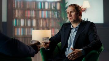Investor consultant engage in meaningful conversation with friend, enjoying fine scotch and making propositions for new business opportunity at elite social club. Camera B. photo