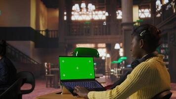 Black scholar reading information via internet next to chroma key in library, focusing on theoretical studies and completing class assignments. Taking notes for educational work. Camera A. photo