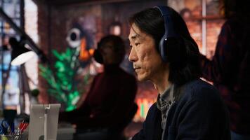 AI startup office chief technology officer listening music while coding application. Senior programmer wearing headphones, working in artificial intelligence software development agency, camera B photo