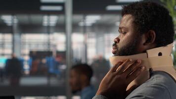 Black general manager suffering from neck injury, wears cervical foam, struggling with uncomfortable position at desk. Analyst trying to solve daily tasks but being in pain. Camera A. photo