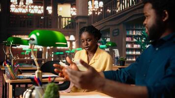 African american scholars reading course notes and comparing information at the library, studying for test together using academic database for research. Educational materials. Camera A. photo