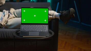 Freelancer laying on couch with music next to mockup display on pc, feeling happy with flexible work schedule at home. Young adult uses tablet relaxing on sofa. Camera A. photo