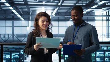 Data center management executives reading paperwork files, reviewing system diagnostics. Server farm colleagues looking over maintenance schedules and cybersecurity protocols, camera B photo