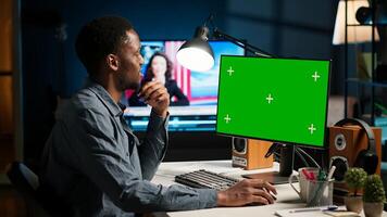 African american person working from home, checking green screen on PC, enjoys remote job at home office setup. Teleworker multitasking and networking in modern loft. Camera B. photo