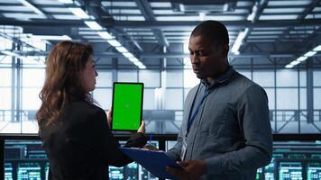 Computer scientists in data center use mockup tablet, inspecting server rigs, updating devices. IT colleagues collaborating to ensure stable operations, using chroma key device, camera B photo