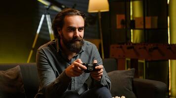 Excited man holding controller in apartment, playing videogames. Happy gamer on couch using joystick to participate in PvP game on console system, relaxing and having fun, camera A photo