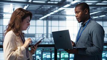 Team of technicians working in server farm, using laptops to analyze data. Coworkers examining infrastructure in data center, ensuring system integrity and security, camera B photo
