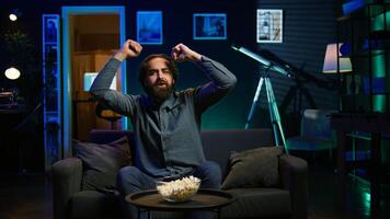 Ecstatic sports fan watching live match at home, shouting to celebrate favorite team scoring. Euphoric man yelling and doing frantic hand gestures, delighted about goal, camera B photo