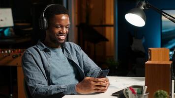 African american person takes break from work to answer texts at home, using smartphone to scroll social media apps. Young guy enjoying remote job, listening to music on device. Camera B. photo