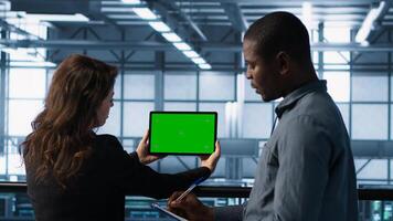 System administrators in server farm using isolated mockup tablet to verify settings. Data center colleagues using green screen chroma key device to monitor facility, camera A photo