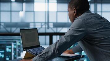 Technician coding on laptop, managing server virtualization and finetuning network protocols. Server farm employee programming on notebook, enforcing advanced security measures, camera A photo