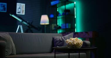Apartment room with dimmed lighting, popcorn and remote on small table, creating relaxed mood for movie night, close up. Panning shot of snack bowl on table in living room photo