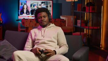 African american man plays intense online games at home, spamming attack buttons on controller. Gamer participating in virtual competition, playing on gaming console. Camera A. photo