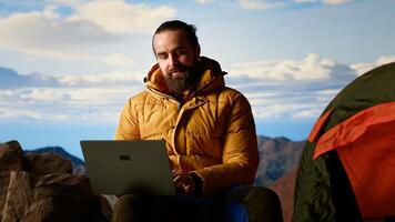 Workaholic explorer always connected and addicted to uninterrupted work, opening laptop on mountain top. Young hiker with internet dependency enjoys strong signal. Camera B. photo