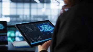 Data center technician using artificial intelligence on tablet to prevent vulnerabilities. Employee using device to review firewall, enforcing AI cybersecurity protocols, camera B close up photo