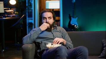 Man at home looking in disbelief at thriller film on TV, stuffing mouth with popcorn. Stupefied person watching suspenseful movie on VOD channel, perplexed by plot twist, camera A photo
