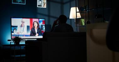 Curious spectator reading news coverage titles on smart tv, sitting on couch and listening to journalist lay out recent global events. Guy watching daily news headlines. Camera A. photo