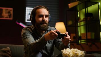 Excited man playing videogames using controller, having fun in living room. Enthusiastic gamer competing in multiplayer game using gamepad, talking with friends through headset, camera A photo