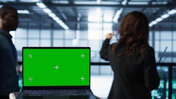 Mockup laptop in front of software developers walking in data center, reviewing equipment diagnostics. Close up of isolated screen notebook next to IT professionals in server farm photo