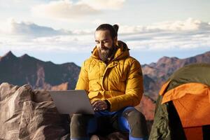Young explorer keeps working at top of mountain with internet everywhere, enjoying global connectivity and productivity on hill summit. High speed strong signal during hike. photo