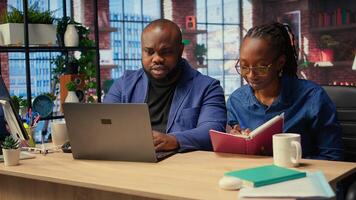 Woman completing spreadsheets on notebook, writing numerical data into cells, calculating totals. African american couple analyzing online information for accounting task. Camera A. photo